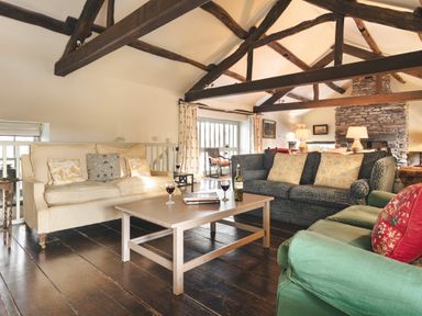 A living room with sofas coffee table wine glasses exposed wooden beams and a stone fireplace at High Lindeth in Bowness
