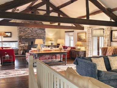 A living room with exposed wooden beams stone fireplace multiple sofas and table lamps at High Lindeth in Bowness