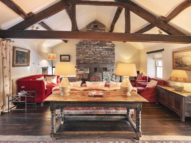 A living room with wooden beams stone fireplace and red sofas at High Lindeth in Bowness