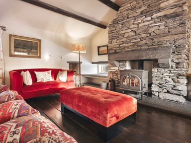 A living room with a stone fireplace red sofa and ottoman and patterned armchair at High Lindeth in Bowness