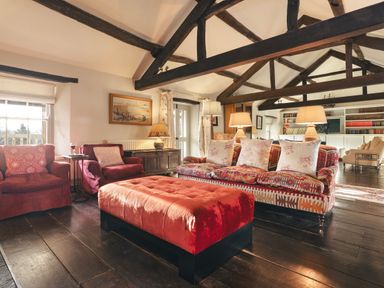 A living room with exposed wooden beams red chairs a patterned sofa and a red ottoman at High Lindeth in Bowness