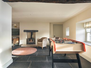 A room with a foosball table a wicker chair a fireplace and a round rug at High Lindeth in Bowness