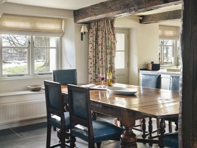 A dining area with a wooden table and blue leather chairs near windows and a door with floral curtains at High Lindeth in Bowness