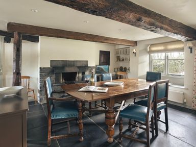 A dining room with a wooden table and blue chairs near a fireplace at High Lindeth in Bowness
