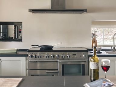 A kitchen with a stainless steel oven stove microwave and a bottle of red wine with a glass at High Lindeth in Bowness