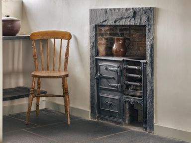 A wooden chair next to a black cast iron stove with a brown jug on top at High Lindeth in Bowness