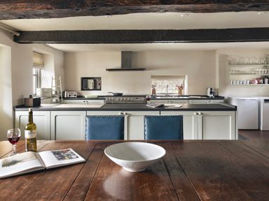 A kitchen with a wooden table a white bowl a wine bottle and glass a stove and shelves with cups at High Lindeth in Bowness