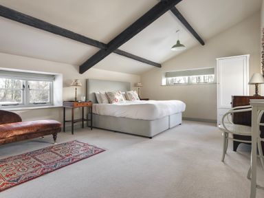 A bedroom with a double bed bedside tables a chair a rug and exposed ceiling beams at High Lindeth in Bowness
