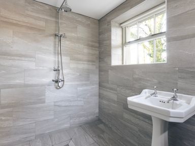 A bathroom with a wall-mounted shower and a white pedestal sink under a window at High Lindeth in Bowness