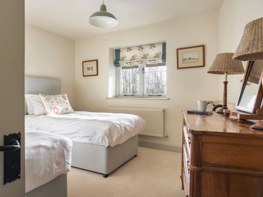 A bedroom with two single beds a wooden dresser with lamps and a window with floral curtains at High Lindeth in Bowness