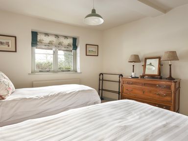 A bedroom with two single beds a wooden dresser with lamps and a mirror and a window with floral curtains at High Lindeth in Bowness