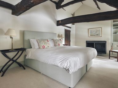 A bedroom with a large bed two bedside tables with lamps exposed wooden beams and a fireplace at High Lindeth in Bowness