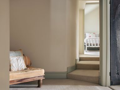 A beige cushioned wooden bench in a hallway with three carpeted steps leading to a bedroom with a white bed at High Lindeth in Bowness