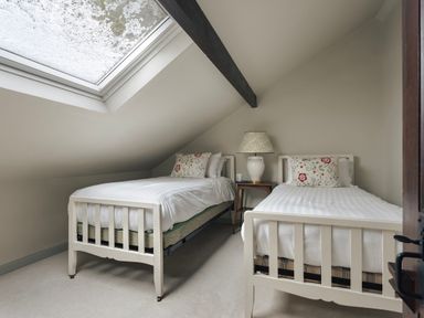 A bedroom with two single beds a skylight and a bedside table with a lamp at High Lindeth in Bowness