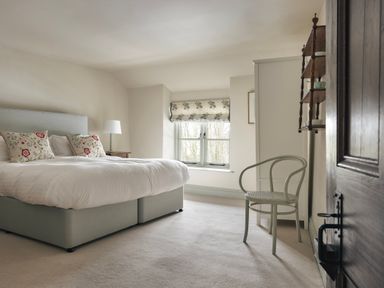 A bedroom with a bed with floral pillows a chair a window and a shelf at High Lindeth in Bowness