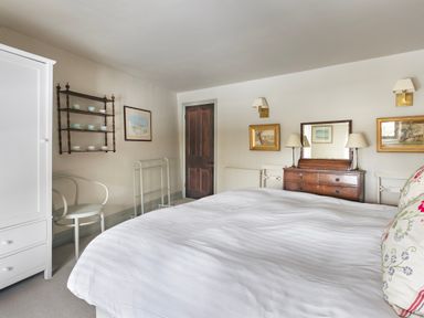 A bedroom with a white wardrobe a wooden door a wooden chest of drawers with a mirror and lamps two chairs and a bed with white bedding at High Lindeth in Bowness