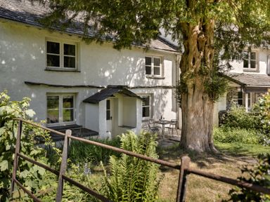 The exterior of a white building with windows a small porch a large tree and a table with two chairs on a patio at High Lindeth in Bowness
