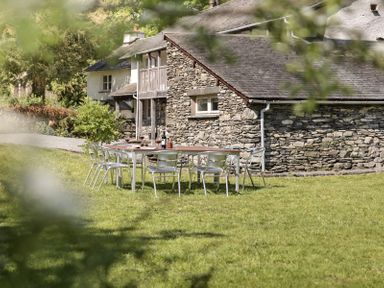 An outdoor dining table with chairs on a lawn next to a stone house at High Lindeth in Bowness