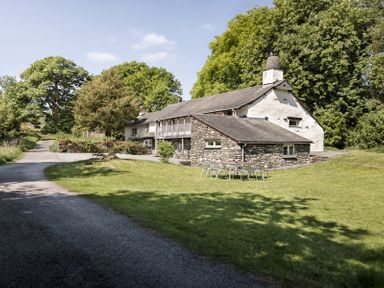 A country house with a stone extension and outdoor metal table and chairs on a lawn at High Lindeth in Bowness