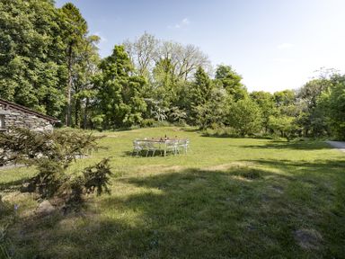 An outdoor grassy area with a table and chairs surrounded by trees at High Lindeth in Bowness