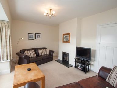 A living room with two leather sofas a wooden coffee table a television on a stand a fireplace and framed pictures on the wall at The Haven in Keswick