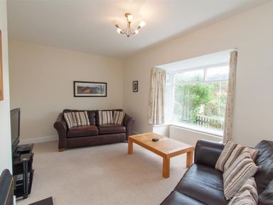 A living room with two leather sofas facing a wooden coffee table and a large window with curtains at The Haven in Keswick