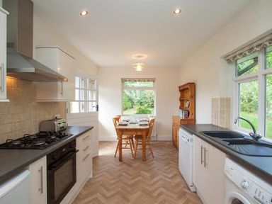 A kitchen with a wooden dining table and chairs a stove a sink dishwasher washing machine and a wooden cabinet at The Haven in Keswick