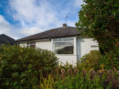 A white house with a tiled roof surrounded by bushes and a wooden fence at The Haven in Keswick