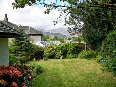 A backyard garden with grass lawn shrubs trees and a house roof with mountains in the background at The Haven in Keswick