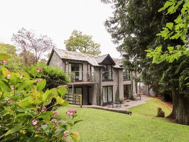 A two-story house with a balcony and patio surrounded by trees and grass at Fir Howe in Skelwith