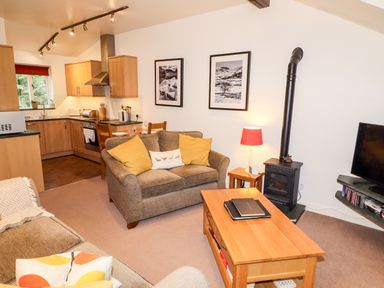 A living room with a sofa wooden coffee table and a wood stove next to an open kitchen at Fir Howe in Skelwith