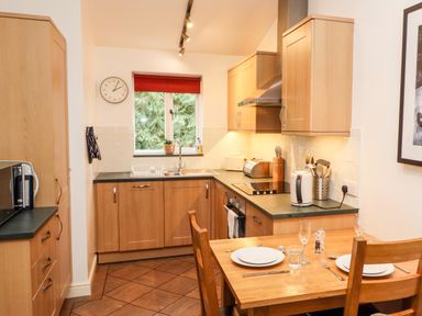 A kitchen with wooden cabinets a dining table set with plates and glasses and a window with a red blind at Fir Howe in Skelwith