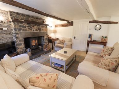 A living room with a stone fireplace a wood-burning stove sofas with cushions a coffee table and wooden beams at Syke Cottage in Hawkshead