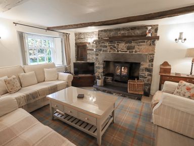 A living room with a stone fireplace a TV sofas and a coffee table at Syke Cottage in Hawkshead