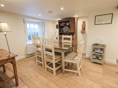A dining room with a wooden table and six chairs a wooden cabinet and a small side table with glassware at Syke Cottage in Hawkshead