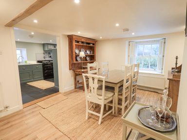 A dining room with a table and six chairs wooden cabinet and a window at Syke Cottage in Hawkshead
