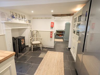 A kitchen with a wood burning stove chair rugs and cabinets at Syke Cottage in Hawkshead