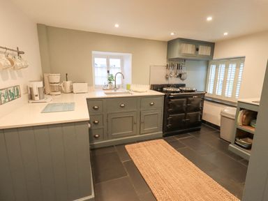 A kitchen with green cabinets a black stove a beige rug and small windows at Syke Cottage in Hawkshead