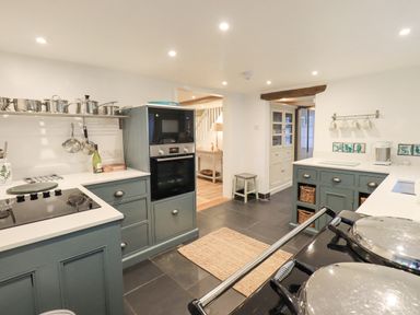 A kitchen with blue cabinets a black stove and oven pots hanging on a wall rack at Syke Cottage in Hawkshead
