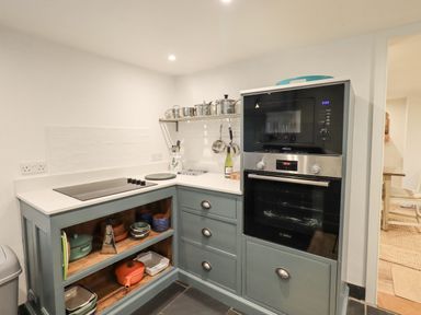 A kitchen corner with an oven microwave unit and open shelves with pots at Syke Cottage in Hawkshead