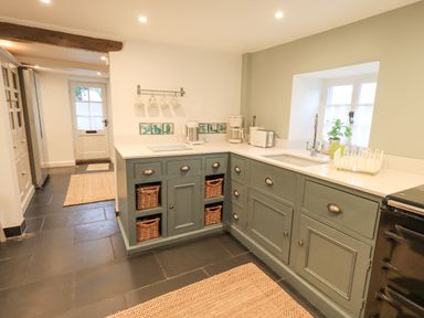 A kitchen with green cabinets a white countertop baskets under the counter and a window at Syke Cottage in Hawkshead