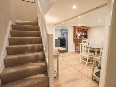 A carpeted staircase next to a dining area with a table and chairs and a wooden cabinet with plates at Syke Cottage in Hawkshead