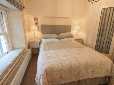 A bedroom with a double bed flanked by two bedside tables with lamps and a window seat at Syke Cottage in Hawkshead