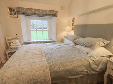 A bedroom with a double bed beside a window with a chair holding folded towels at Syke Cottage in Hawkshead
