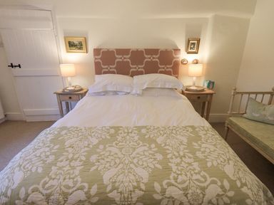 A bedroom with a bed with a patterned headboard two bedside tables with lamps and framed pictures on the wall at Syke Cottage in Hawkshead
