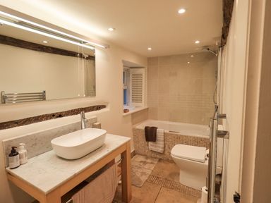 A bathroom with a bathtub shower toilet and a sink on a wooden vanity at Syke Cottage in Hawkshead