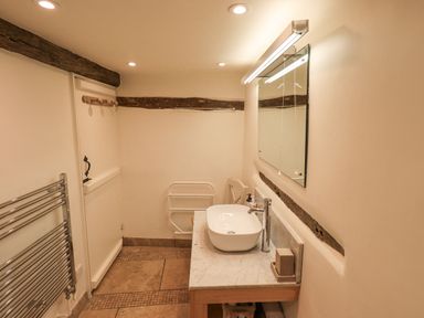 A bathroom with a sink on a wooden countertop a mirror above and wooden beams on the walls at Syke Cottage in Hawkshead