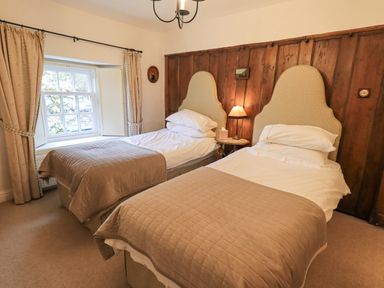 A bedroom with two single beds and a window with curtains at Syke Cottage in Hawkshead
