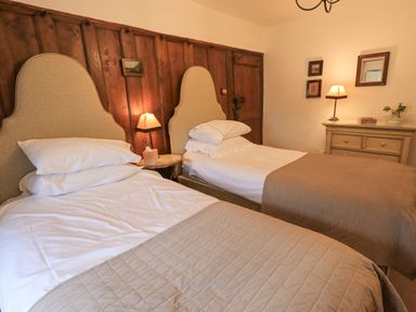 A bedroom with two single beds a wooden panel wall lamps and a dresser at Syke Cottage Hawkshead