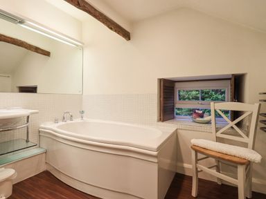 A bathroom with a bathtub a small window with wooden shutters a white chair and a sink at Syke Cottage in Hawkshead